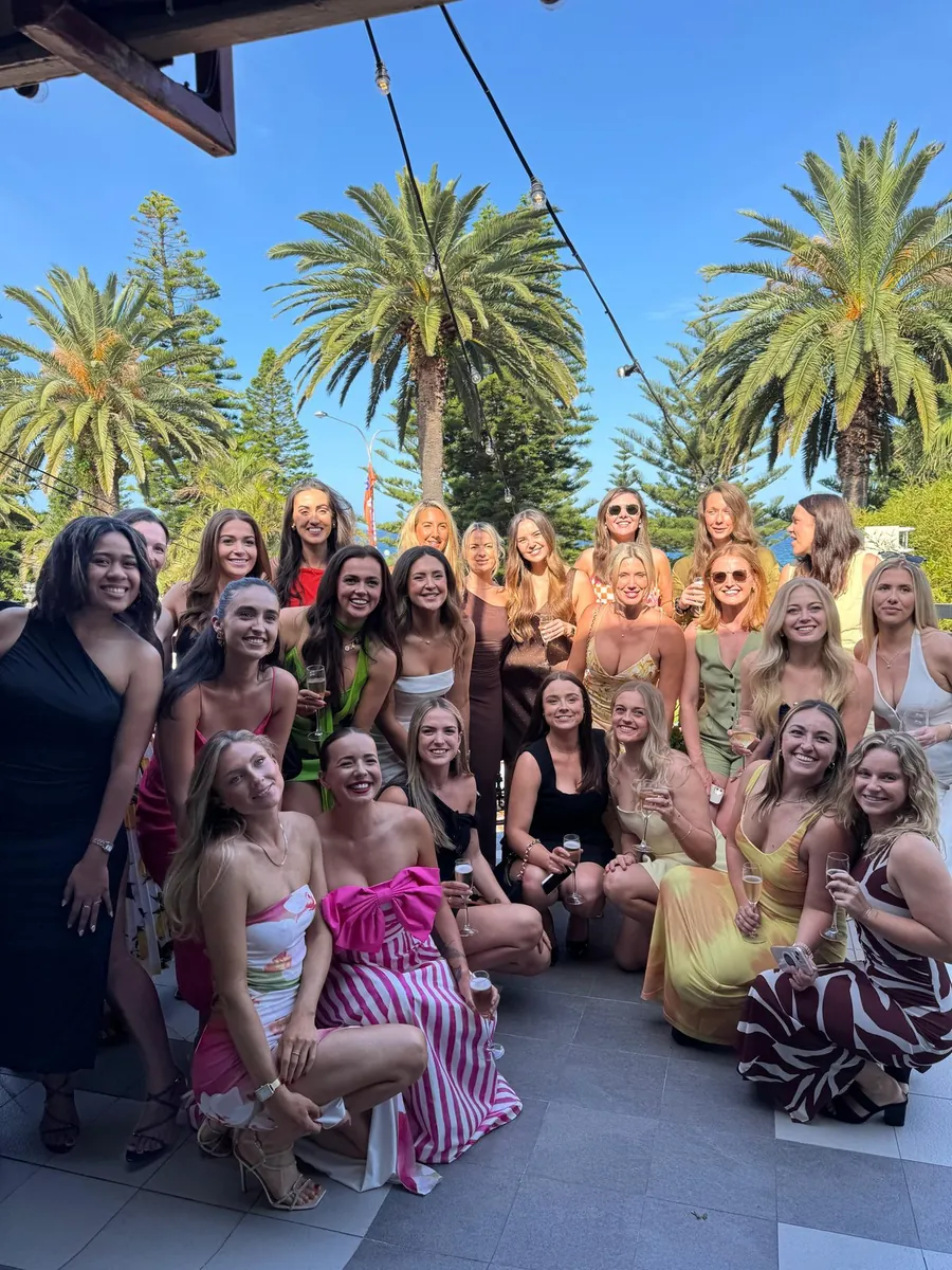 A group of guests in cocktail dresses posing together outdoors on a sunlit patio.